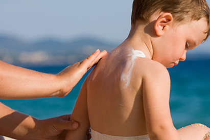 Woman applying sunscreen on a child's back at the beach